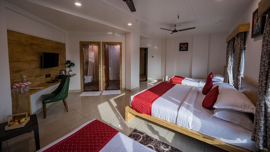 A room at Clarks Collection Somnath with beds, red runners, desk, tv, ceiling fan, chair, table and fruits on the table and wooden decor.