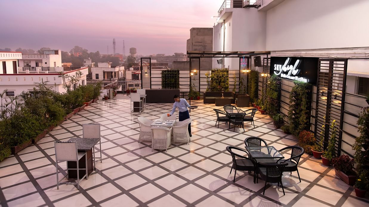  A rooftop terrace offering a stunning view of the city, with comfortable outdoor seating and a tranquil setting with a  man  fixing things on the table - Clarks Inn Express, Near Jammu Bari Brahmana Railway Station