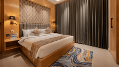 A bright guest room featuring a king-sized bed with a patterned headboard and floor-to-ceiling grey curtains at Ananta Express, Katra.