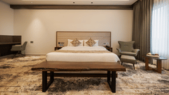 A guest room featuring a king-sized bed, a wooden bench, and a work desk area with an armchair at Ananta Express, Katra.