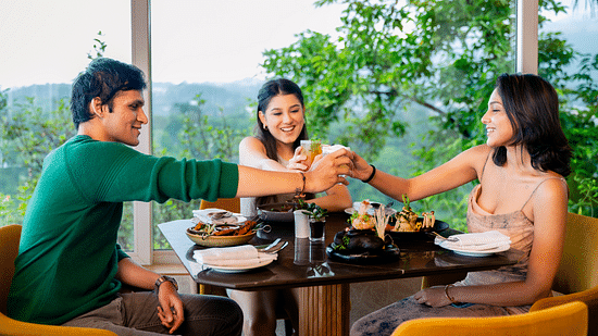 An image of three people sitting in a cafe clinging there glasses together with an amazing view behind them - The Dukes Retreat, Khandala