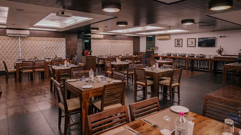 The dining area with wooden tables, chairs neatly arranged water bottles, spoons and plates at Clarks Collection, Vadodara.