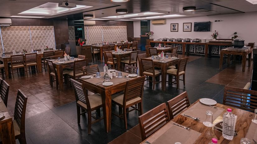 The dining area with wooden tables, chairs neatly arranged water bottles, spoons and plates at Clarks Collection, Vadodara.