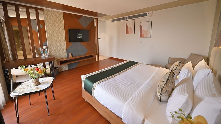 A bedroom with a bed facing a wall-mounted television and a table with a flower vase placed beside the bed at  Clarks Collection Grand Sapphire, Ajmer