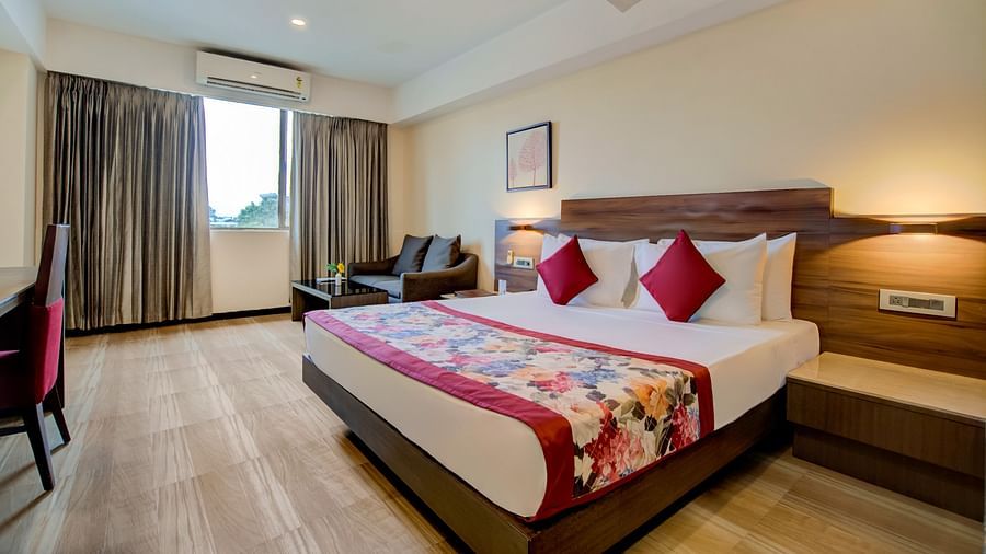 Spacious room with a double bed, lounge chairs, and natural light from large windows at Voyage Milestone Hotel and Banquet Siliguri
