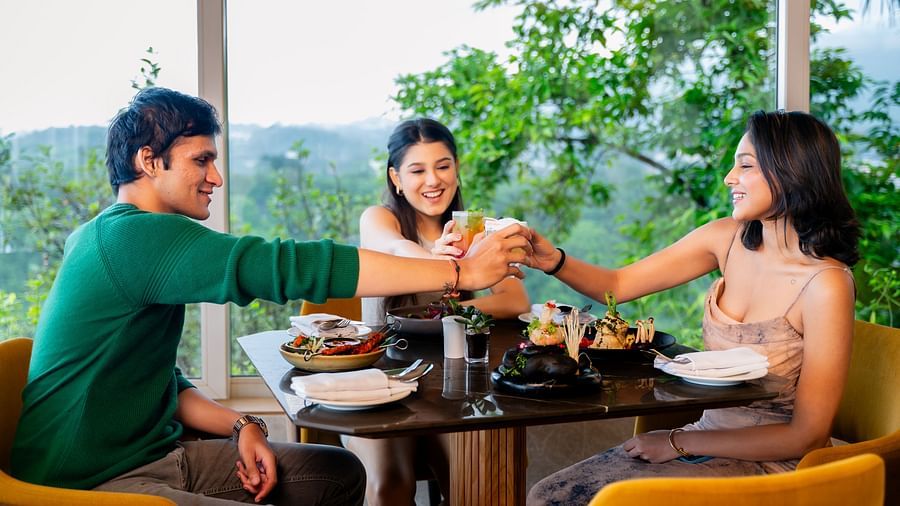 An image of three people sitting in a cafe clinging there glasses together with an amazing view behind them - The Dukes Retreat, Khandala