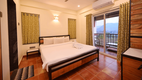 This bedroom at Forest Escapes Koyna is equipped with a bed, ceiling fan, and a view through large windows.