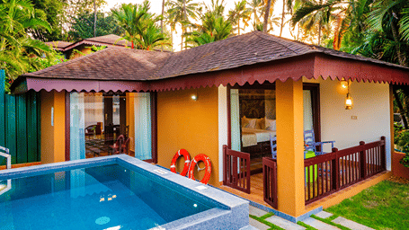 A villa exterior with a swimming pool in the foreground and lush greenery in the backdrop.