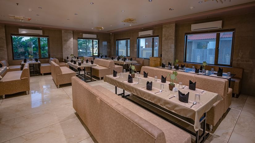 The lounge-style seating area with cushioned arm sofas, tables wit neatly arranged plates, spoon, glass and elegant lighting at Clarks Collection Somnath.