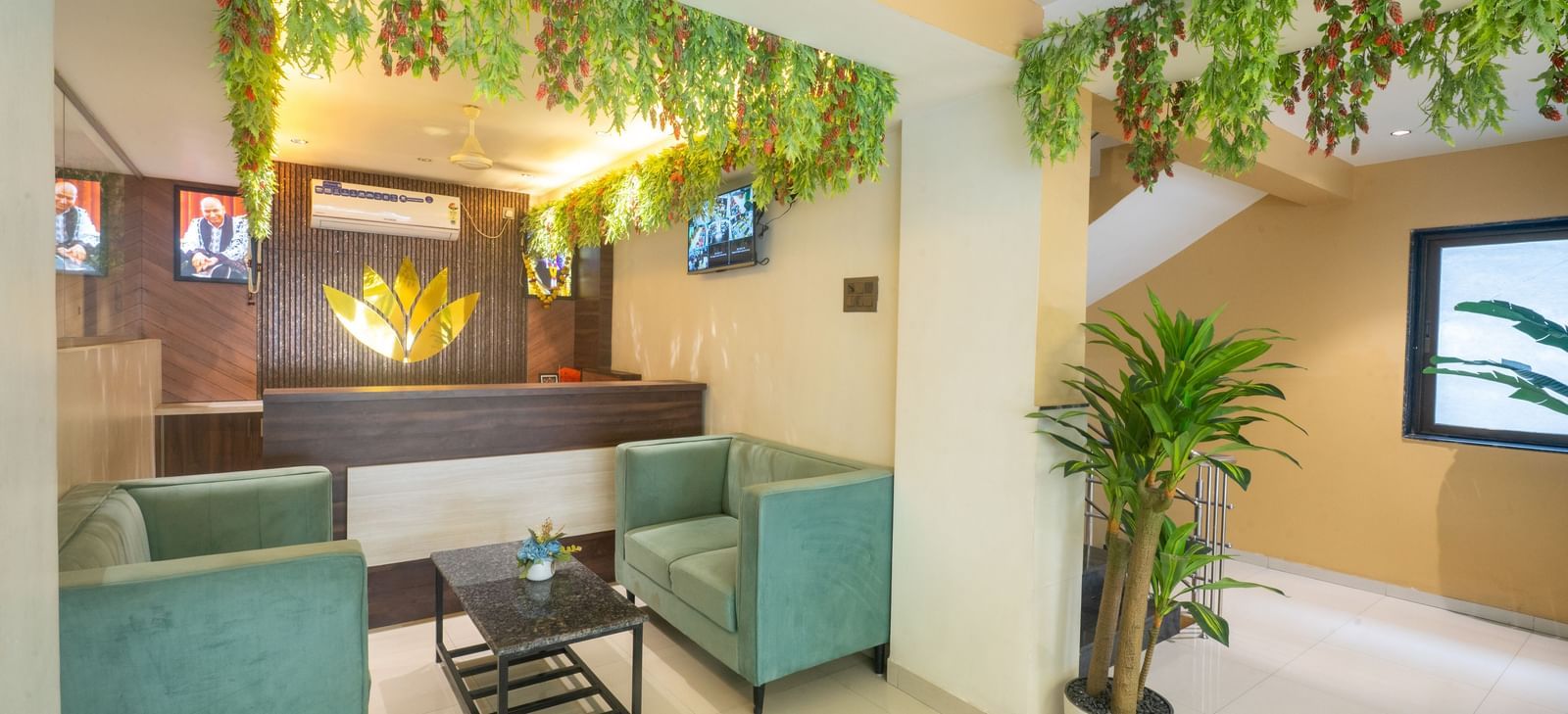 The reception area of Pravasa Stay, Shirdi, has two cushioned chairs and a desk adorned with a gold emblem.