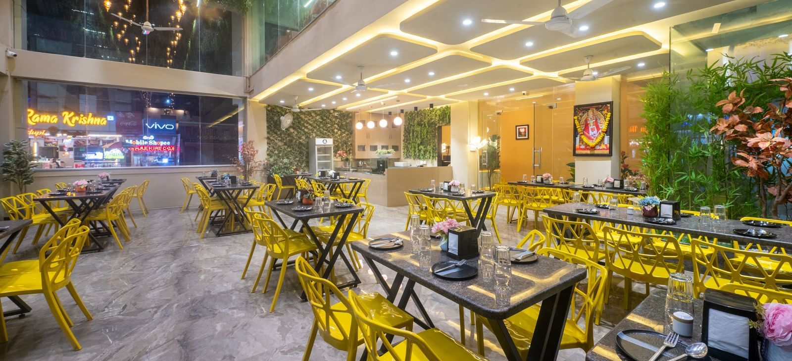 The dining space at Pravasa Stay, Shirdi, features bright yellow chairs and many ceiling lights.