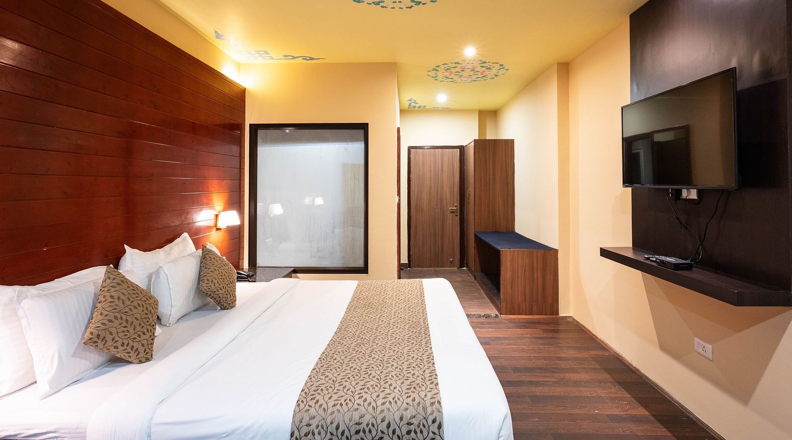 A bedroom featuring a patterned ceiling art and a wall-mounted television at Avianna Hungry Jack, Gangtok.