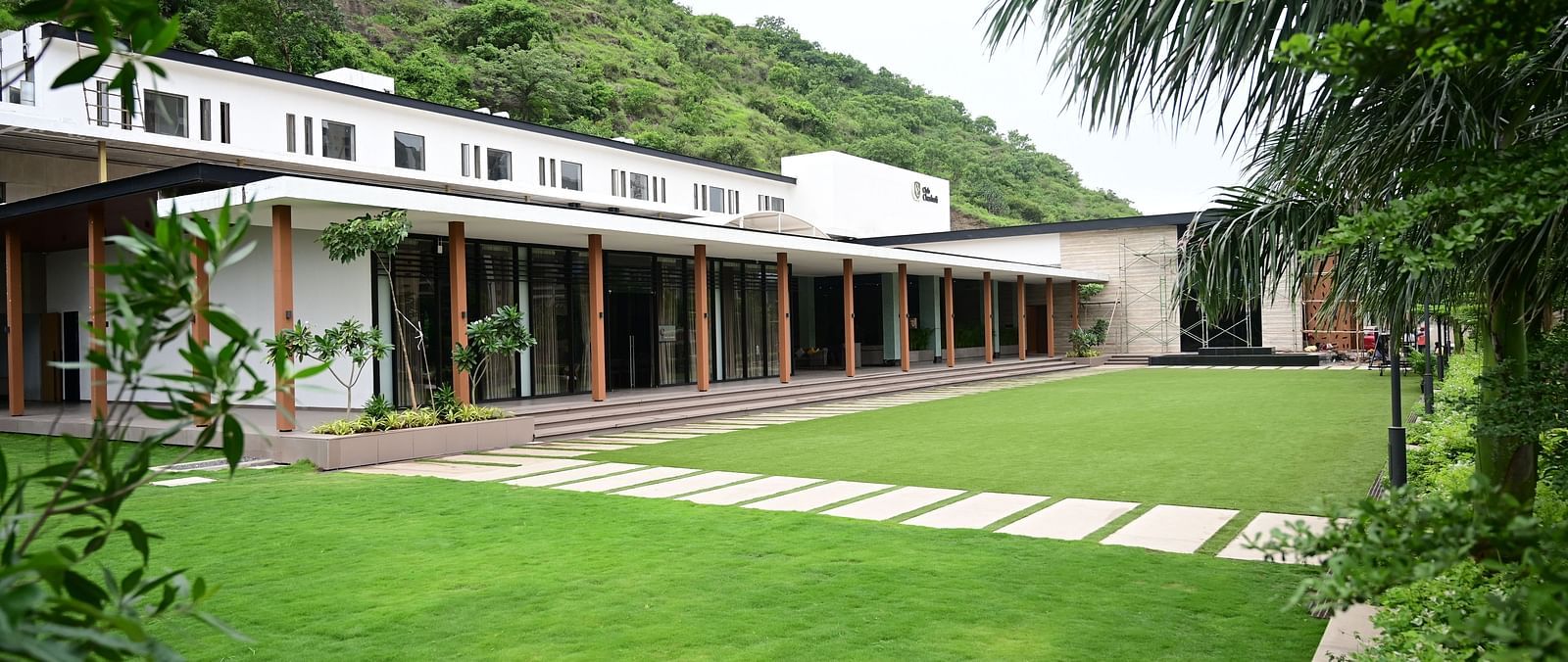 Building with a long porch overlooking a lawn, backed by a wooded hillside.