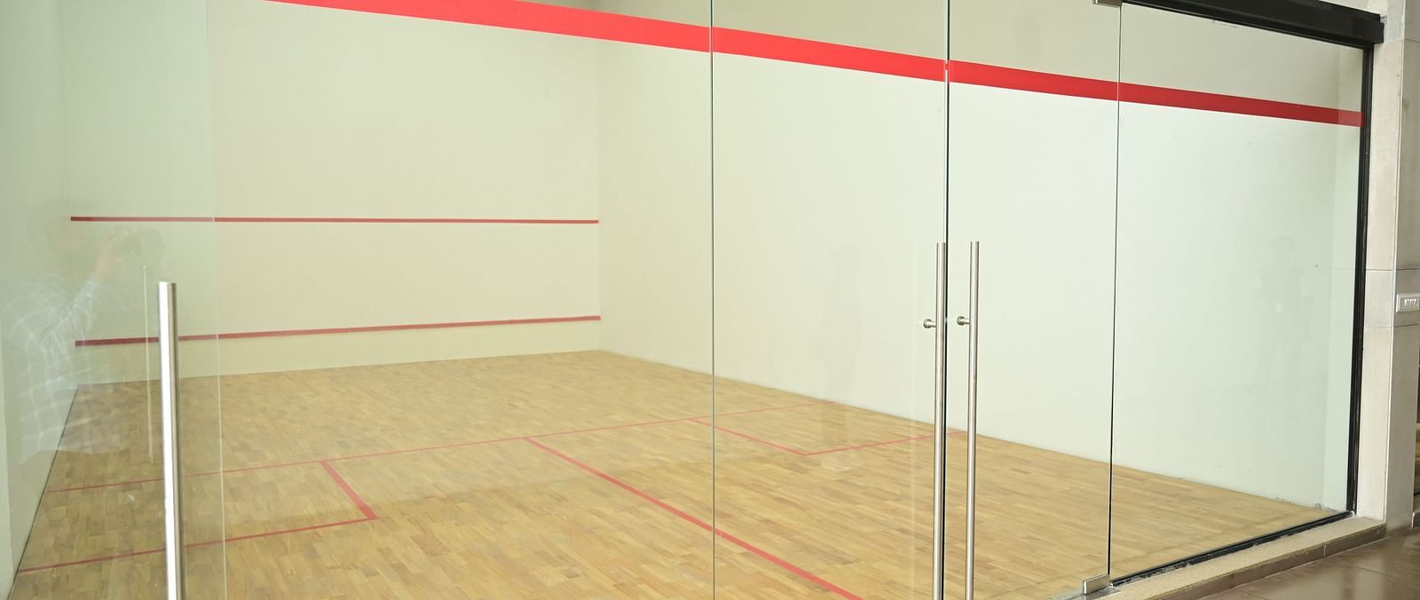 a spacious squash court with tall glass doors at club chrholi, pune