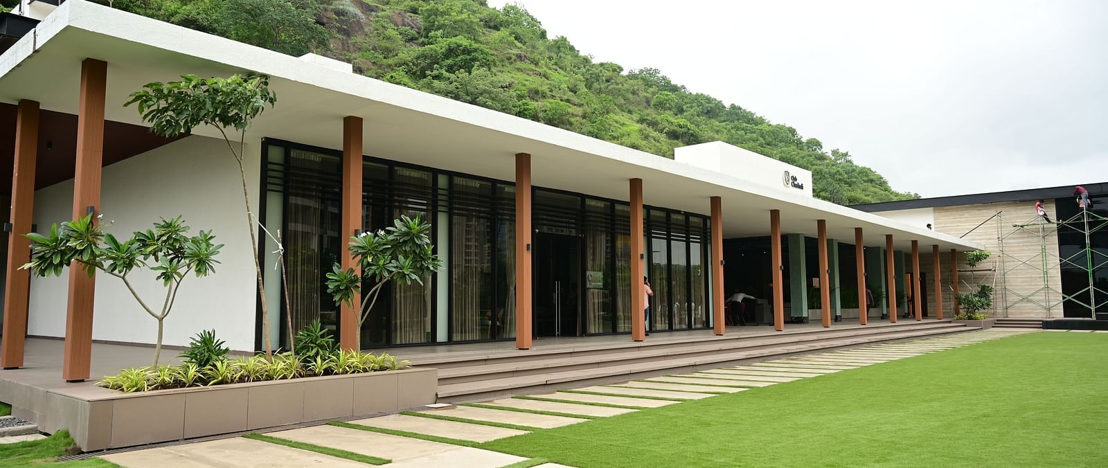 Building with a long, covered walkway, glass doors, and a pathway leading to a lawn and hillside.