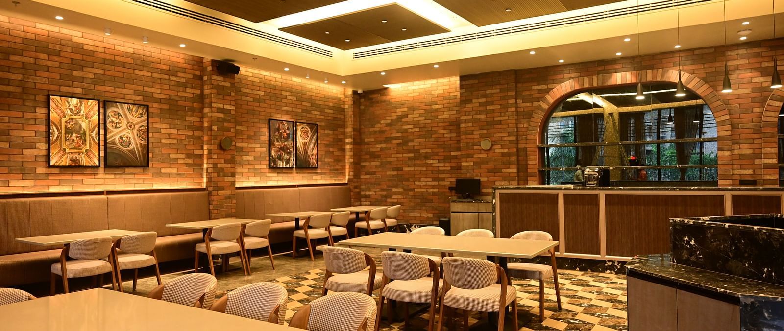 Dining area with tables, chairs, patterned floor, and textured walls, lit by ceiling lights.