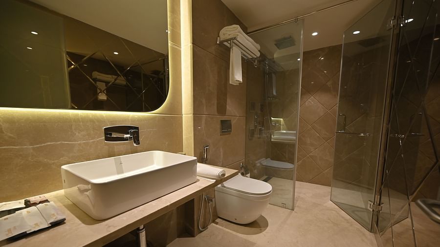 A modern bathroom with a large mirror illuminated by soft yellow lights at Clarks Collection Grand Sapphire, Ajmer.