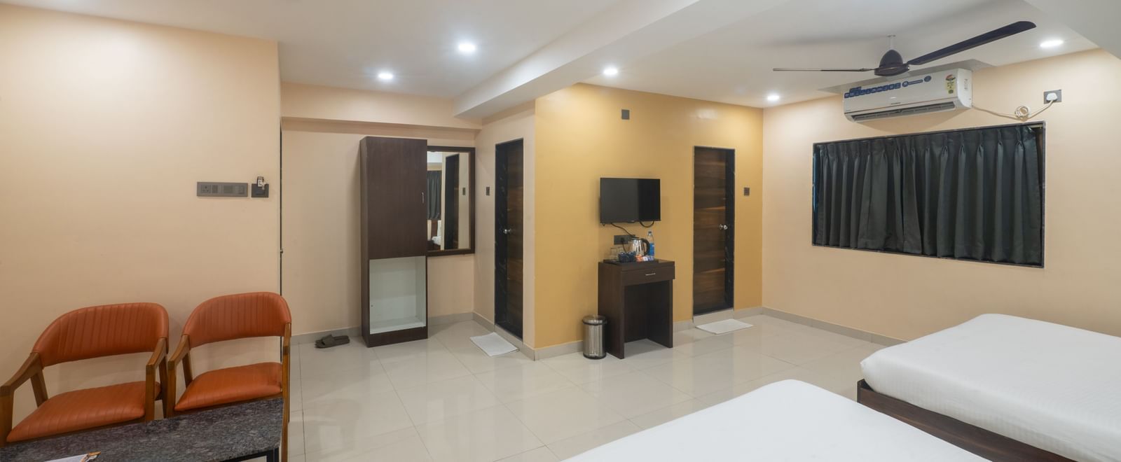 A large room at Pravasa Stay, Shirdi, features two beds, a sitting area, and a wardrobe with a mirror.
