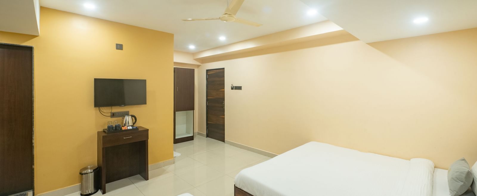 A room at Pravasa Stay, Shirdi, has two beds, a wall-mounted television, and a desk in the corner.