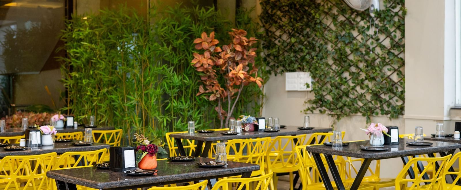The seating area of the Pravasa Stay, Shirdi restaurant is filled with bright yellow chairs and black tables.
