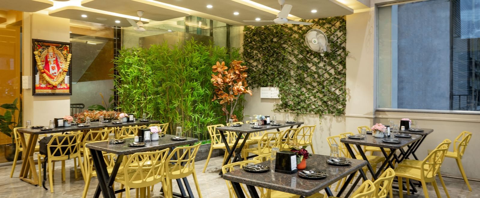 The restaurant at Pravasa Stay, Shirdi, has yellow chairs, black tables, and decorative green walls.