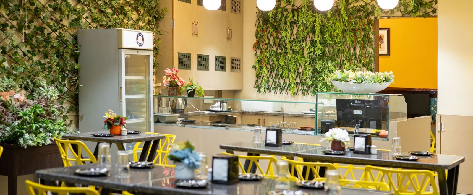 The dining area at Pravasa Stay, Shirdi, features yellow chairs, black tables, and a green living wall decoration.