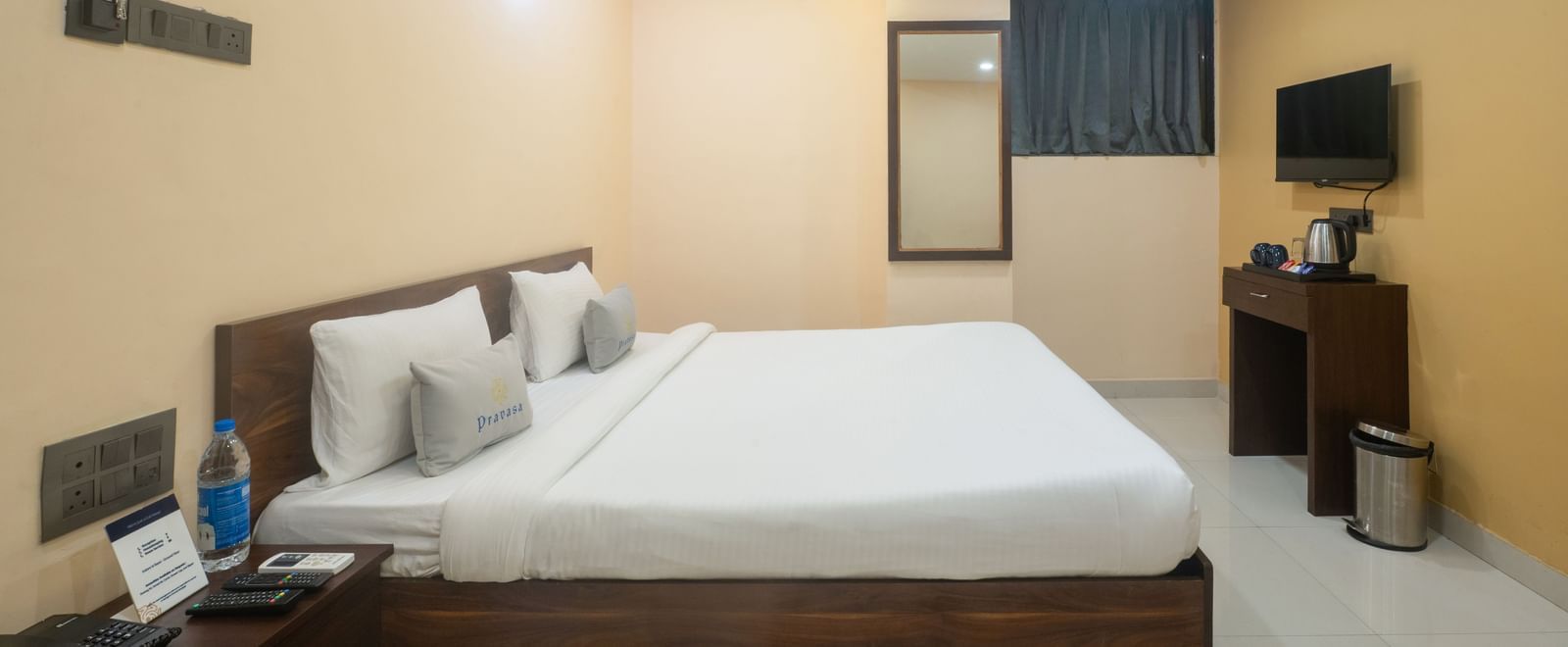This room at Pravasa Stay, Shirdi, features a large wooden bed frame, a mirror, and a television on the opposite wall.