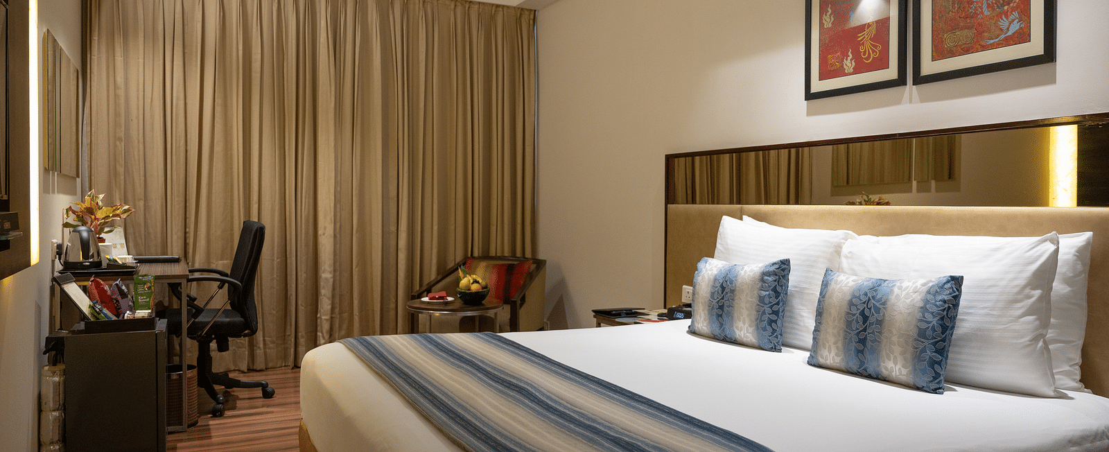 An image of a bedroom with working table and a chair at long shot view of the hotel corridors at Grand Kakinada by GRT Hotels