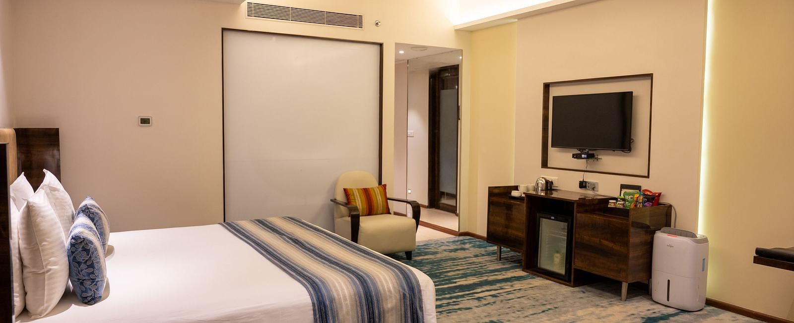 An image of a bedroom with a fan and a wall mounted television at Grand Kakinada by GRT Hotels