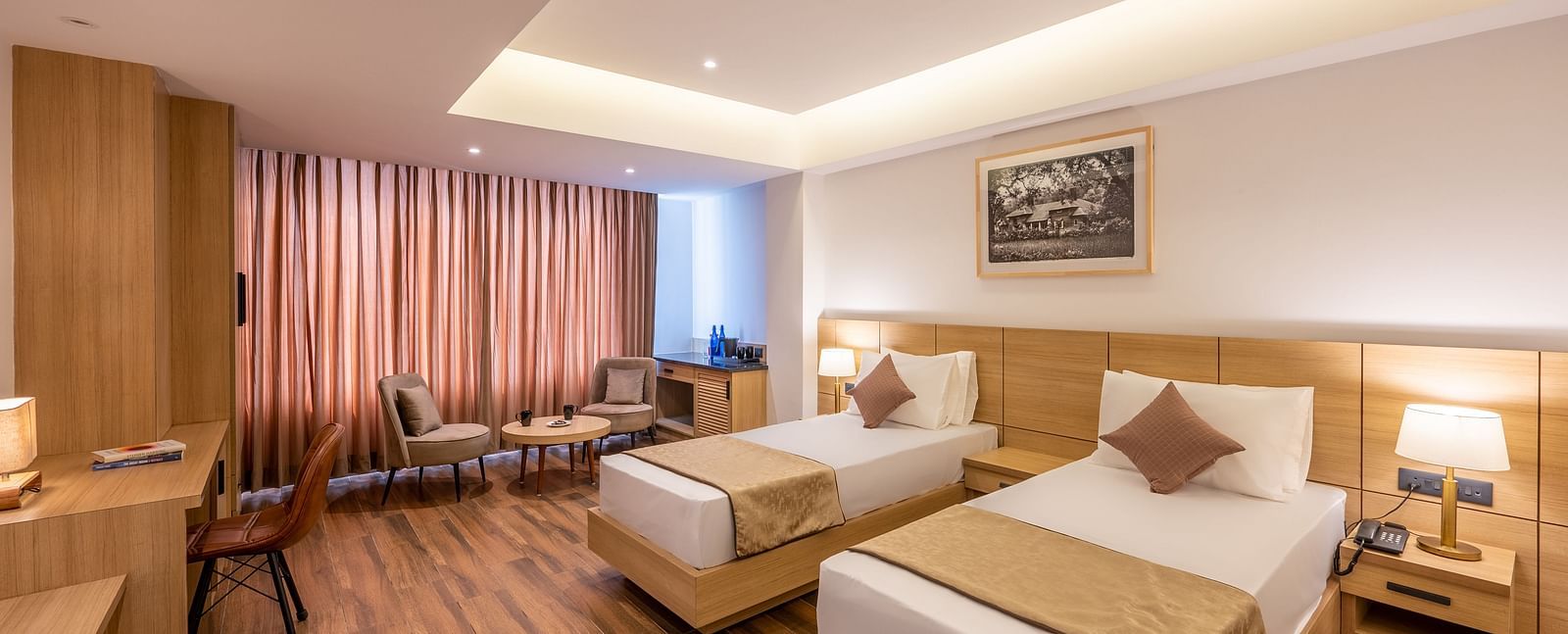 Close up shot of Twin Room at Vishranti Hotel, Dehradun featuring twin beds, side table with bed lamp and a work desk.