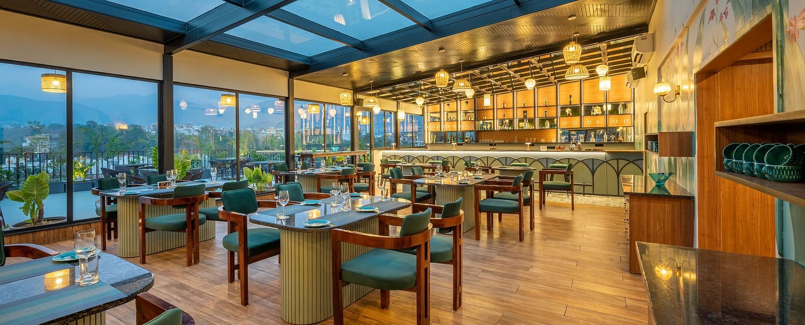 Overview of  interiors of The Gaia Gourmet restaurant at Vishranti Hotel, Dehradun, featuring a well-lit dining area with glass rooftop, wooden floors.