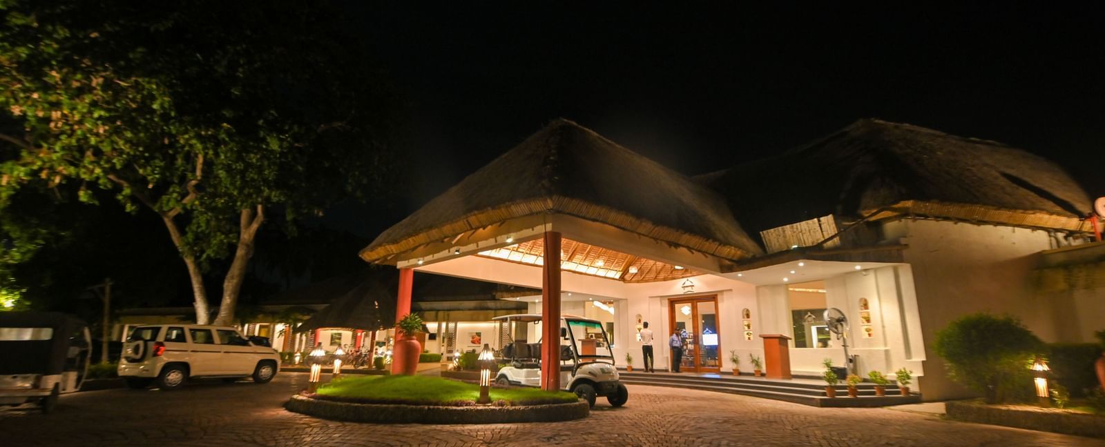 Entrance of Vedic Vilage Spa Resort featuring an internal hotel transportation cart and illuminated resort building.