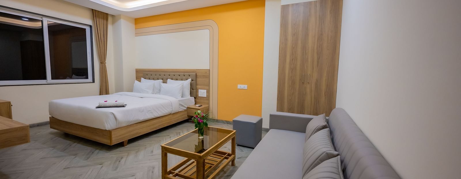 A view of a hotel room with a clean, white bed, a wooden nightstand, and large windows with natural light