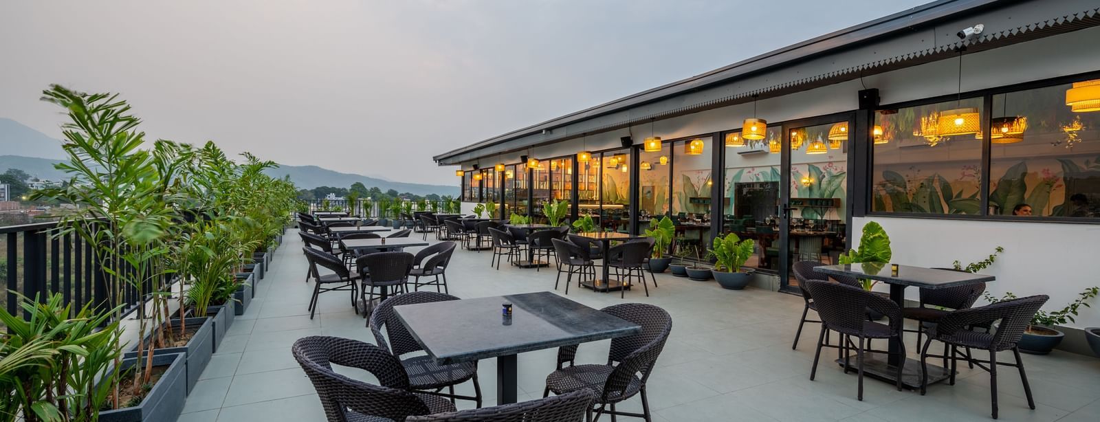 Shot of an outdoor seating area at Vishranti Hotel, Dehradun with a seating area features multiple tables with chairs, and plants are visible in the background.