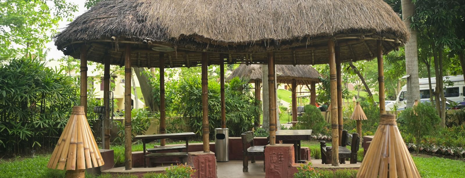 An outdoor dining area in Bhoomi at Vedic Village Spa Resort, featuring a seating space under a thatched roof. 