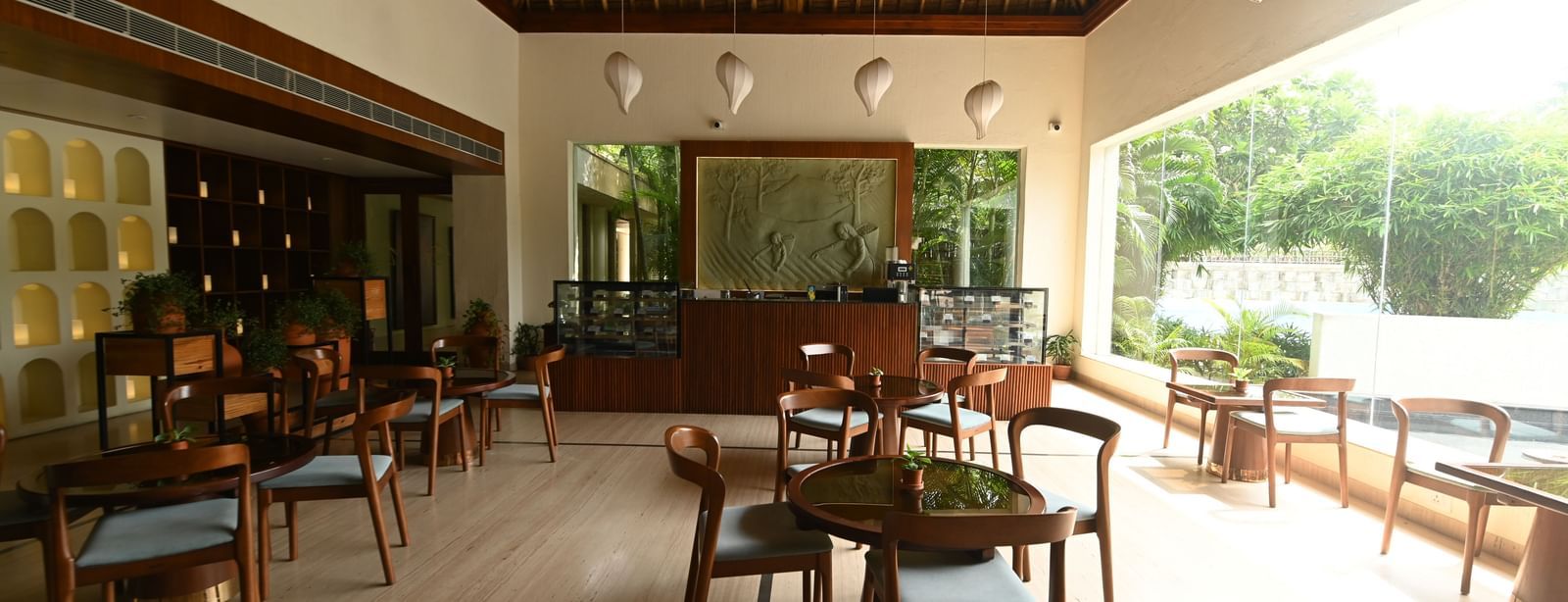 A spacious and elegant indoor dining area with wooden furniture and large windows is shown | Vedic Village Spa Resort, Kolkata