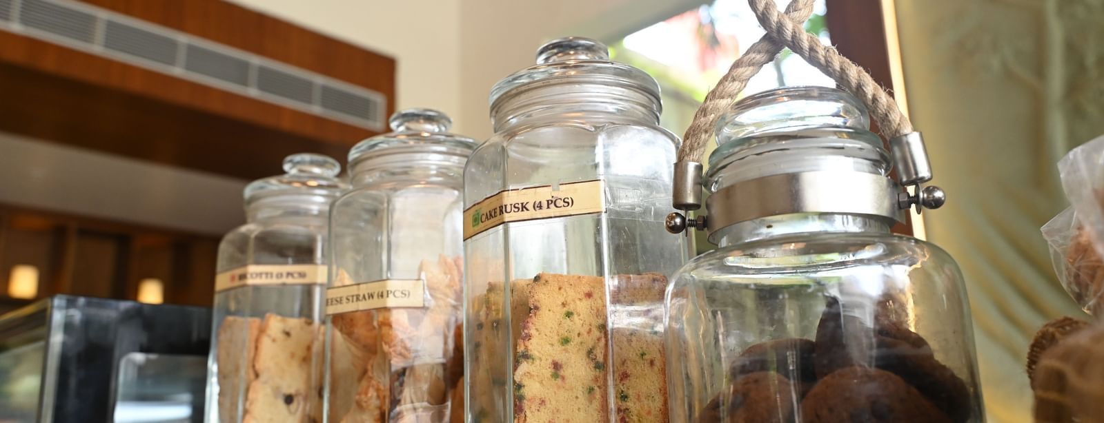 Several clear glass jars filled with various types of cookies are displayed on a shelf in a cafe setting | Vedic Village Spa Resort, Kolkata