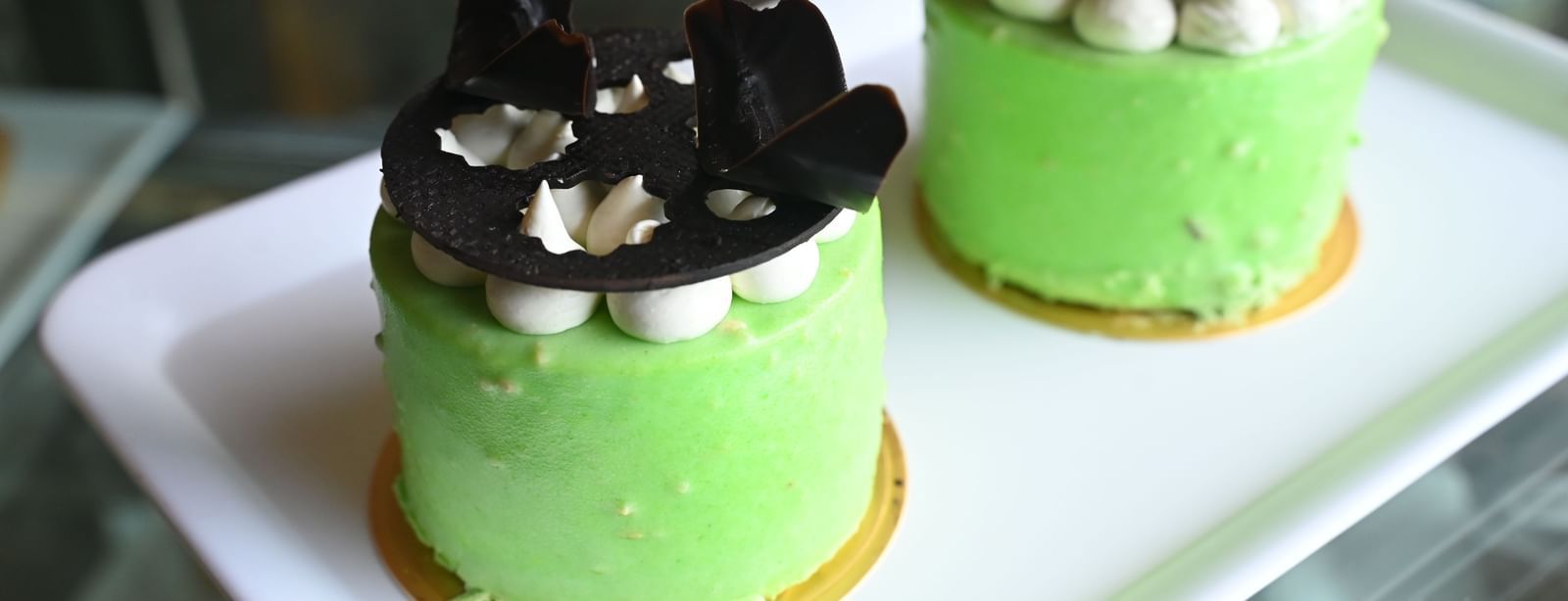 Two vibrant green individual cakes, topped with dark chocolate decorations, are placed on a white serving platter | Vedic Village Spa Resort, Kolkata