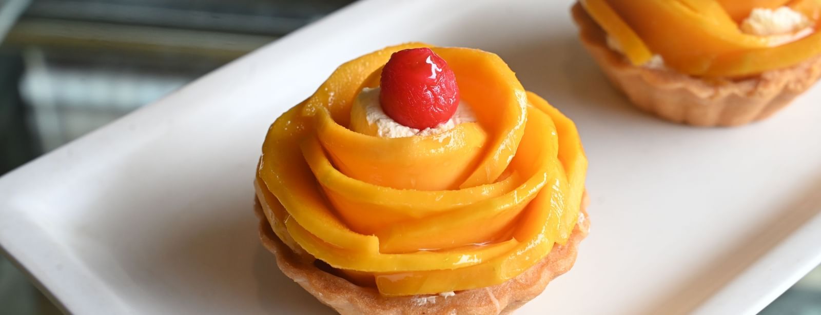 Two mango tarts with a cherry on top are presented on a white plate at Chai | Vedic Village Spa Resort, Kolkata