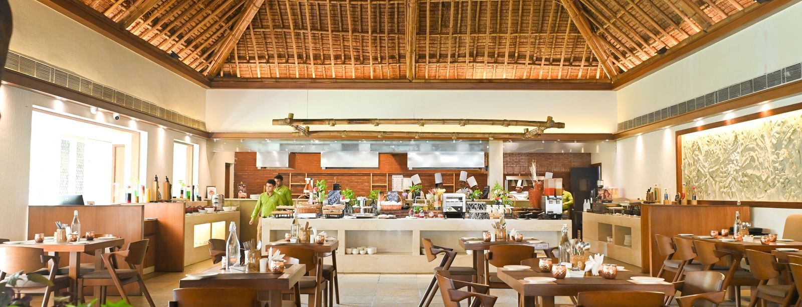 Yagna Restaurant in Vedic Village Spa Resort featuring high thatched ceilings, neatly arranged wooden dining tables and chairs.