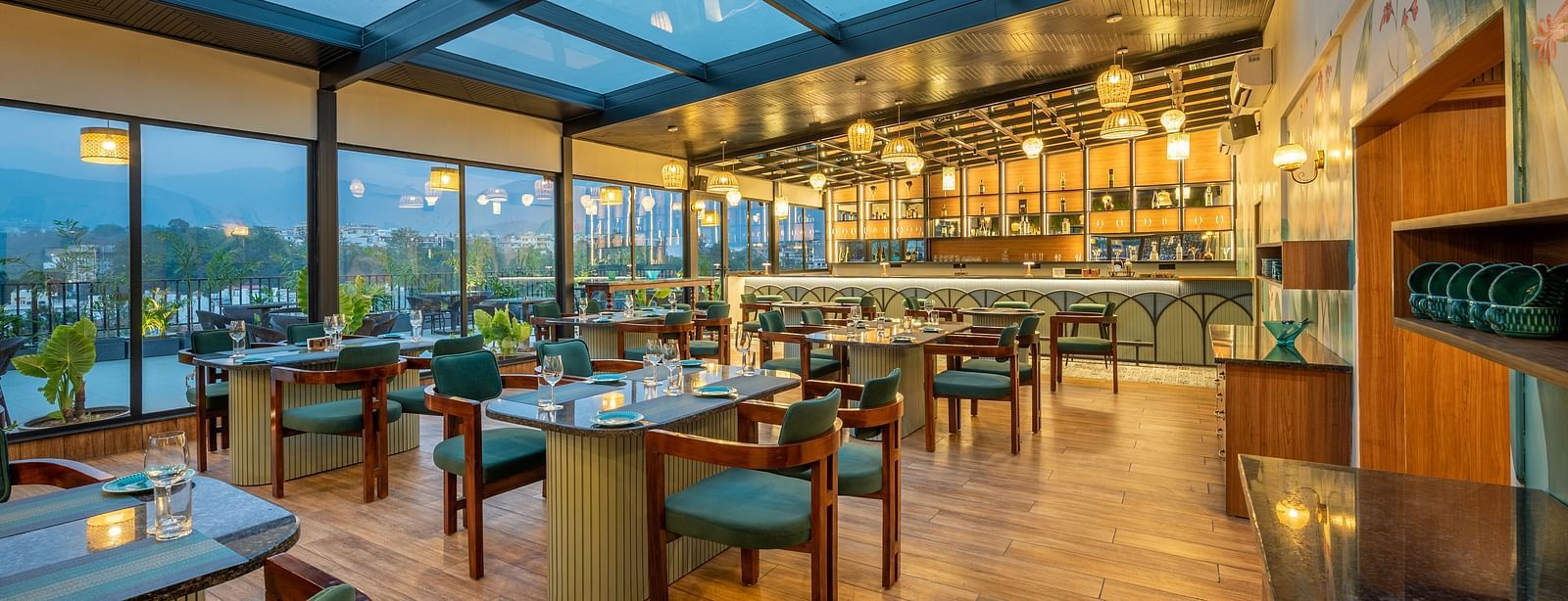 Overview of  interiors of The Gaia Gourmet restaurant at Vishranti Hotel, Dehradun, featuring a well-lit dining area with glass rooftop, wooden floors.