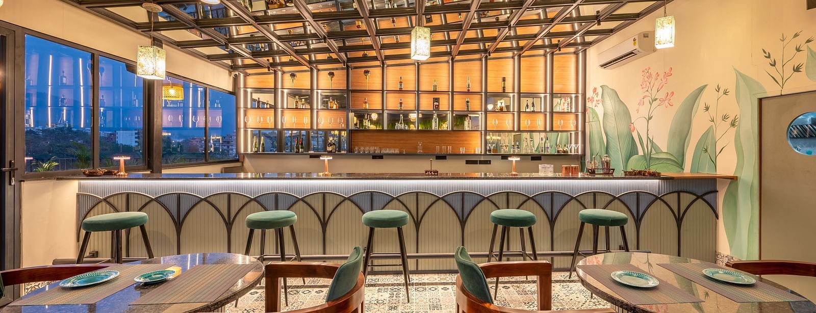 Interior of Bar at Vishranti Hotel, Dehradun, featuring a well-lit bar area with a marble countertop, wooden bar stools, and a variety of bottles displayed on shelves behind the bar.