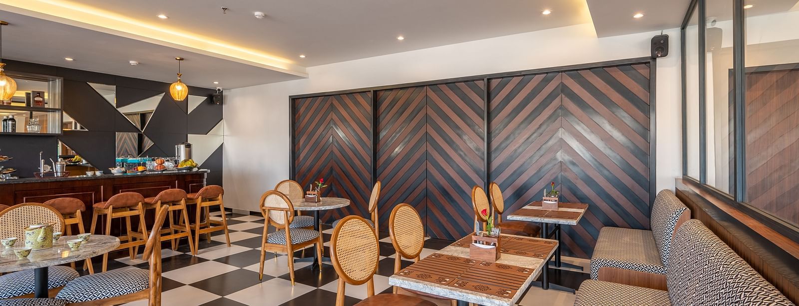 Overview of a bar at Vishranti Hotel Dehradun with chairs, sofas, tables, a counter and checkered floors. 