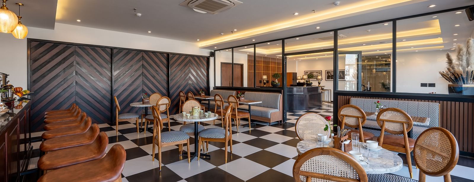 Overview shot of a bar at Vishranti Hotel Dehradun with chairs, tables, a counter and checkered floors. 