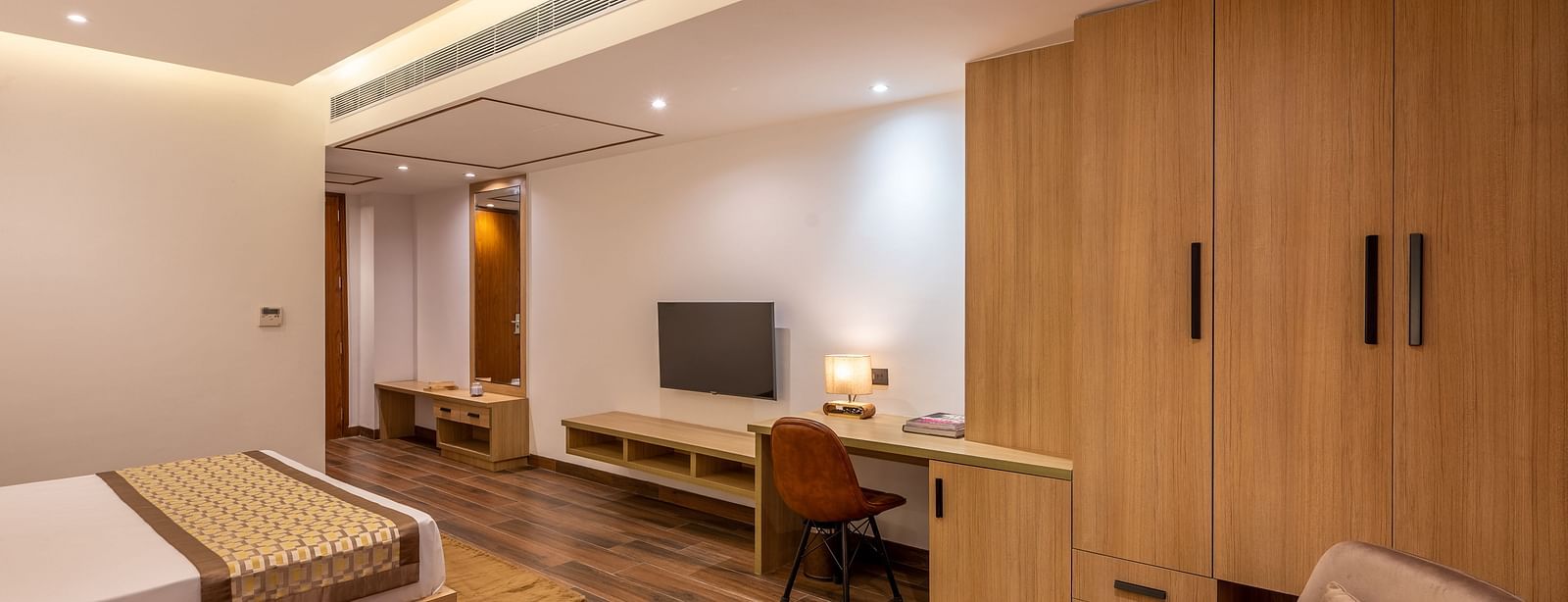 Close up shot of Suite at Vishranti Hotel, Dehradun featuring a king bed with side tables, a TV, large window with curtains and bed lamps. 