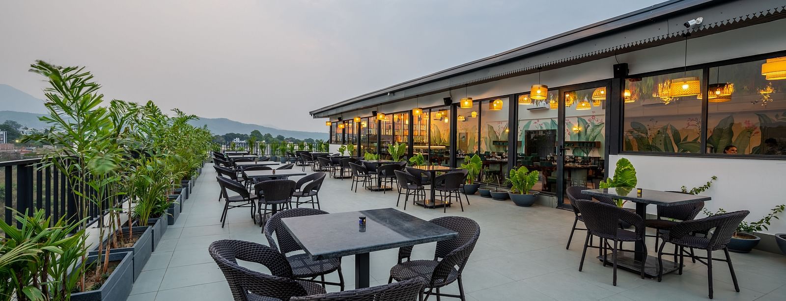 Shot of an outdoor seating area at Vishranti Hotel, Dehradun with a seating area features multiple tables with chairs, and plants are visible in the background.