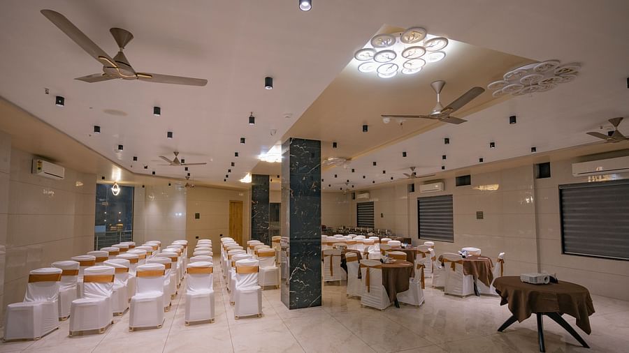 Banquet hall with white covered chairs, fans, round table and chandeliers at Clarks Collection Somnath.