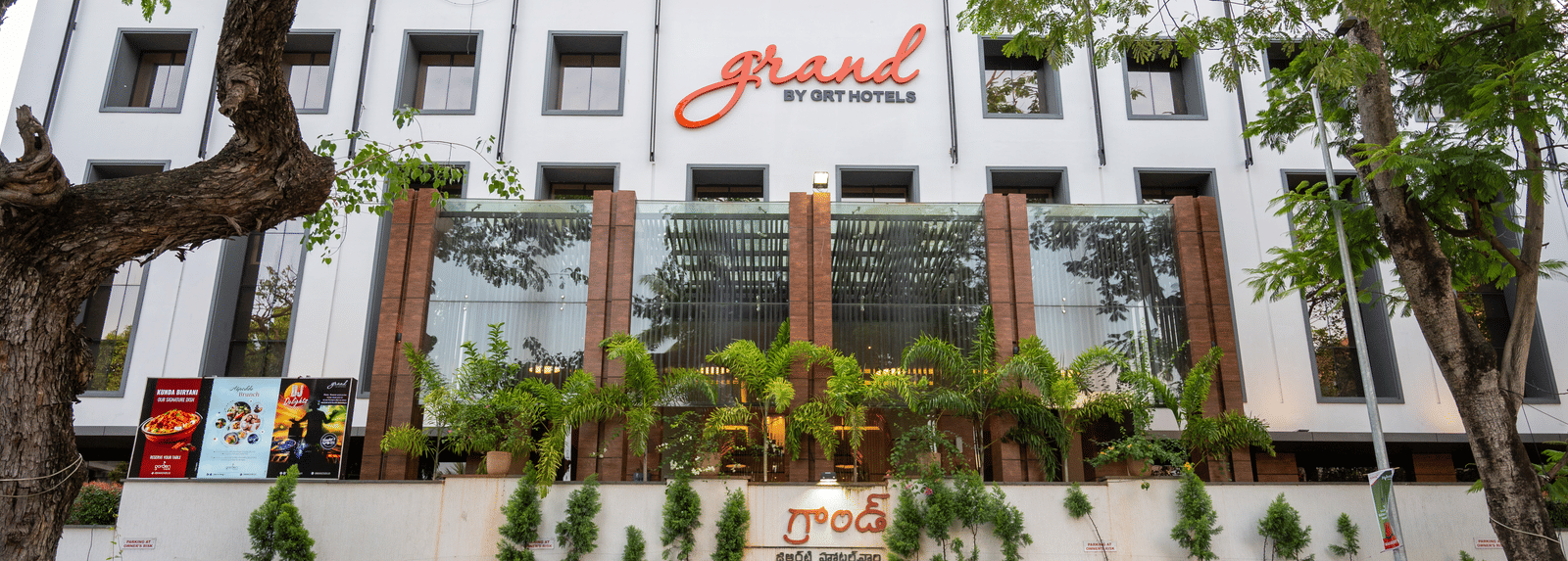 Parking space of Grand Kakinada by GRT Hotels covered with plants and trees