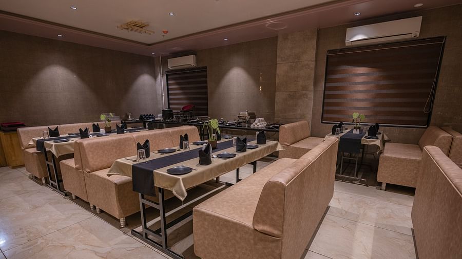 The lounge-style seating area with cushioned arm sofas, tables wit neatly arranged plates, spoon, glass and elegant lighting at Clarks Collection Somnath.