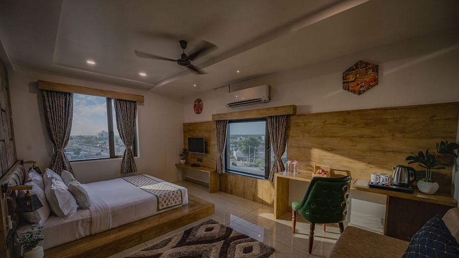 A bedroom at Clarks Collection Somnath featuring a double bed, two windows, ac, chair, study desk, wall-mounted TV, and fan.